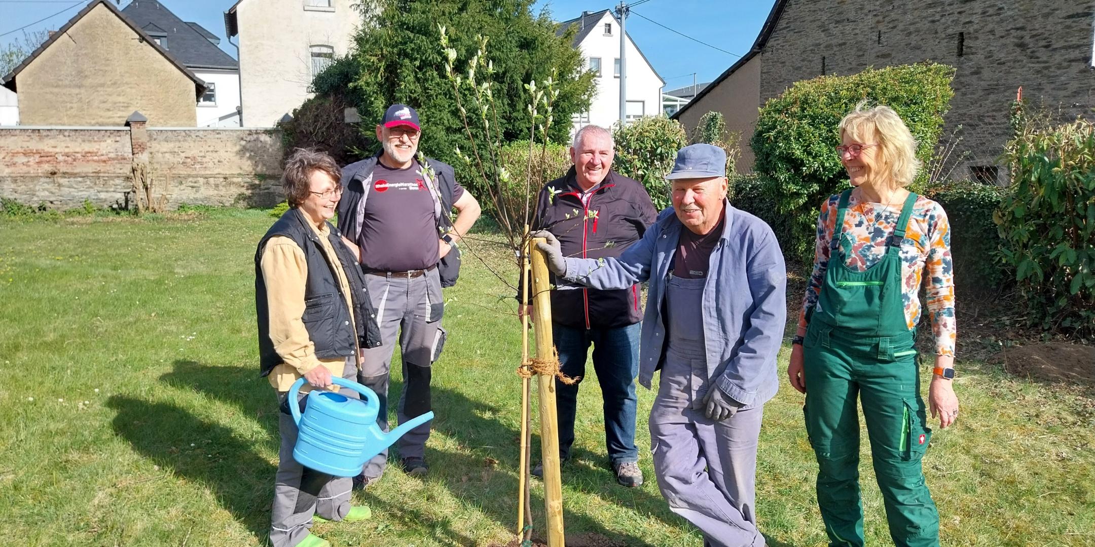 Man sieht ehrenamltiche Helfer, die einen Baum in einem Garten gepflanzt haben