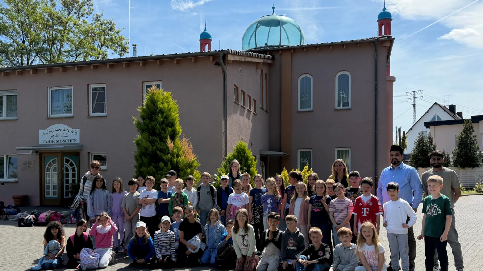 Man sieht eine Gruppe Grundschulkinder bei strahlendem Sonnenschein vor einer Moschee stehen