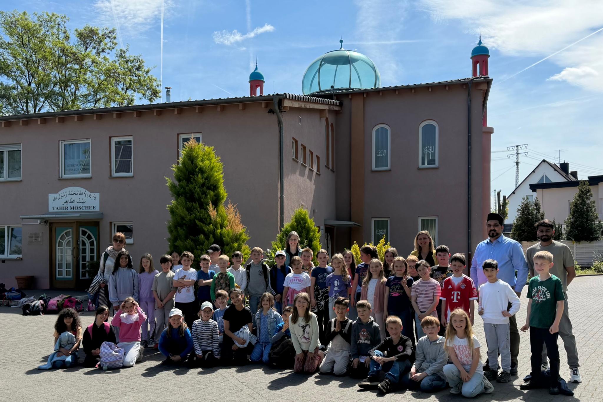 Man sieht eine Gruppe Grundschulkinder bei strahlendem Sonnenschein vor einer Moschee stehen