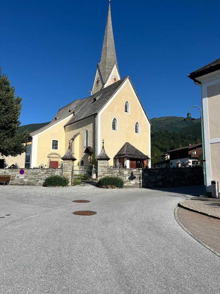 Es sit die gelb gestrichene, mit weiß an den Kanten abgesetzte frühgotische Kirche mit hohem, spitzem Kirchturm vor blauem Himmel zu sehen