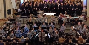 Man sieht den KuBa-Chor im Altarraum der Kirche in Münstermaifeld, davor das Heeresmusikkorps Koblenz mit Instrumenten und in Gala-Uniform