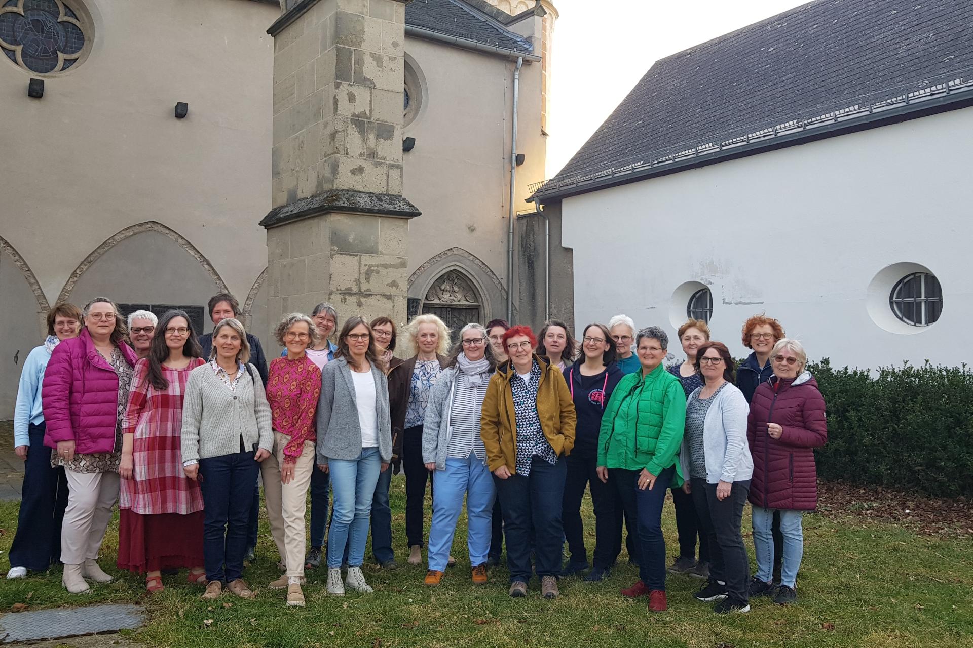 Man sieht die Frauen (Mitglieder) des Chors 'Erdentöne-Himmelsklang' in einem Gruppenfoto vor dem Kreuzgang der Kirche in Münstermaifeld