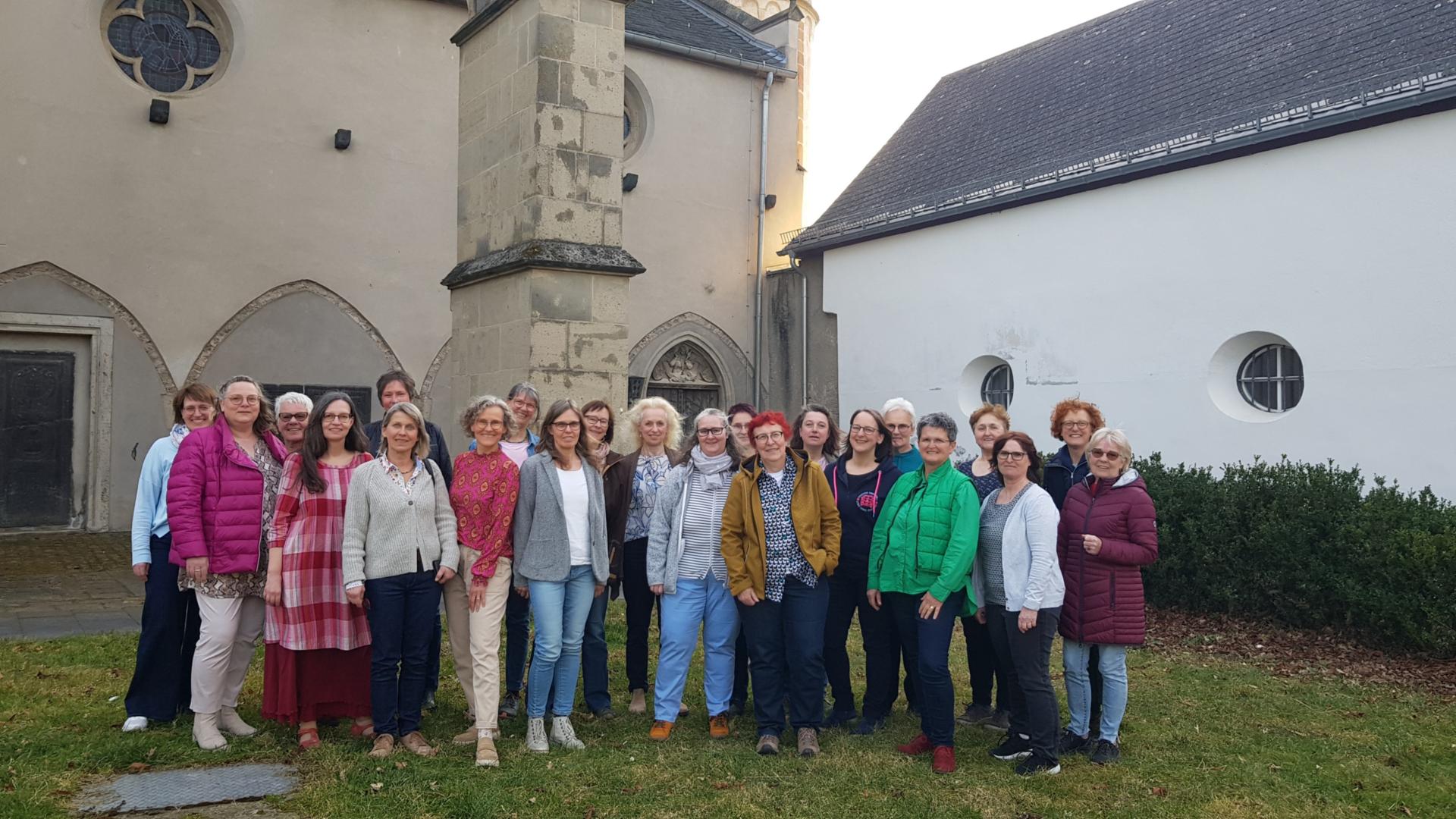 Man sieht die Frauen (Mitglieder) des Chors 'Erdentöne-Himmelsklang' in einem Gruppenfoto vor dem Kreuzgang der Kirche in Münstermaifeld