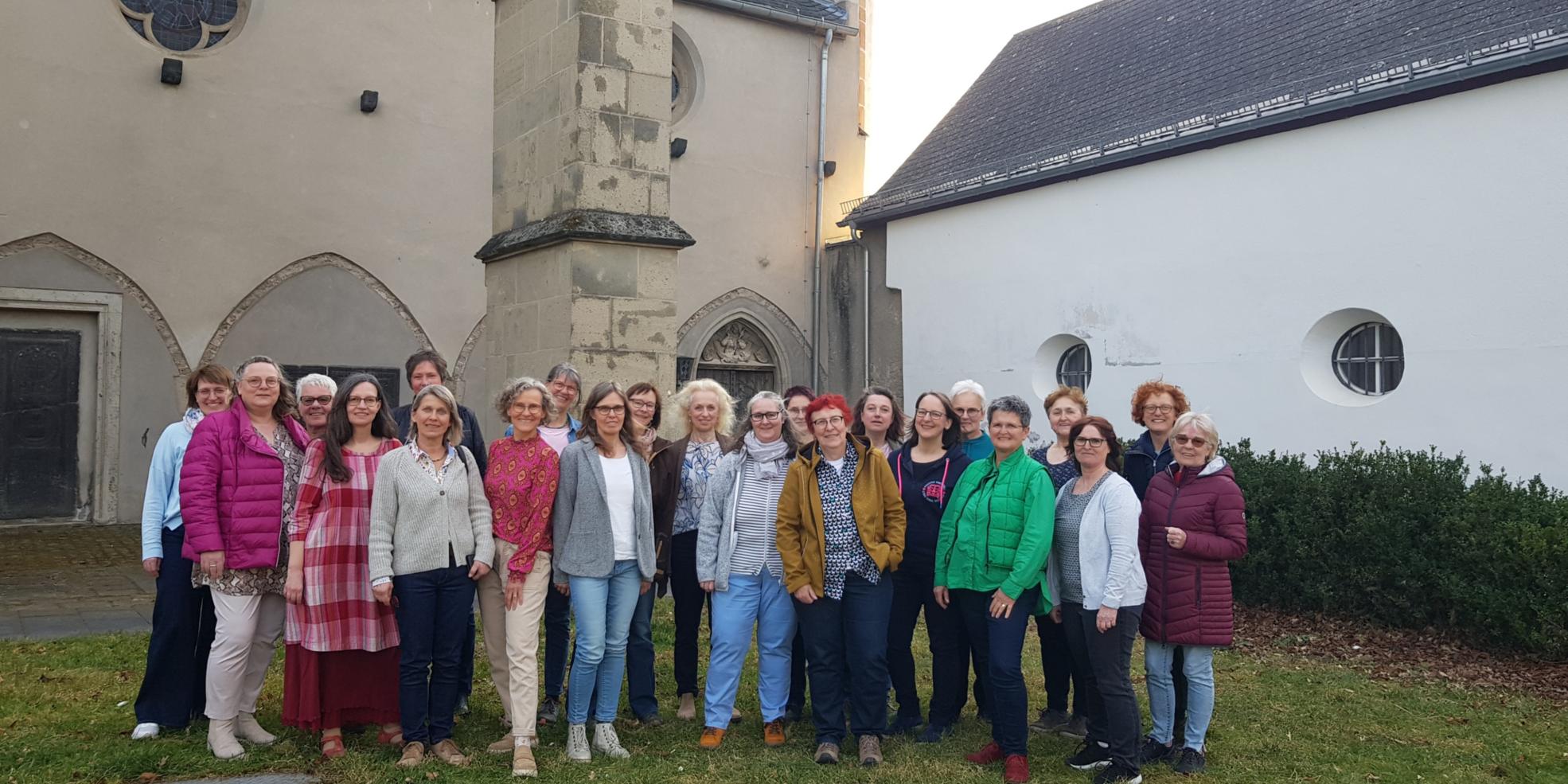 Man sieht die Frauen (Mitglieder) des Chors 'Erdentöne-Himmelsklang' in einem Gruppenfoto vor dem Kreuzgang der Kirche in Münstermaifeld