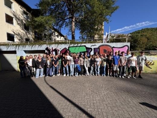 Man sieht eine Gruppe Jugendlicher vor einer mit Grafitti-besprühten Wand stehend