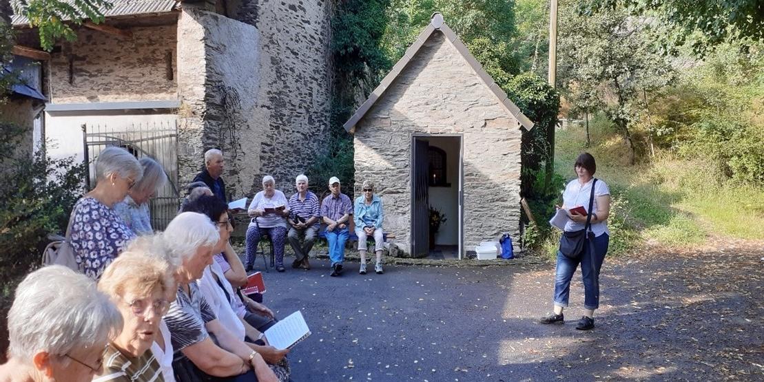 Man sieht eine Frau, die vor einer Gruppe Menschen , die auf Bänken an einer Kapelle sitzen, einen Text vortragen (c) Privat Man sieht eine Frau, die vor einer Gruppe Menschen , die auf Bänken an einer Kapelle sitzen, einen Text vortragen