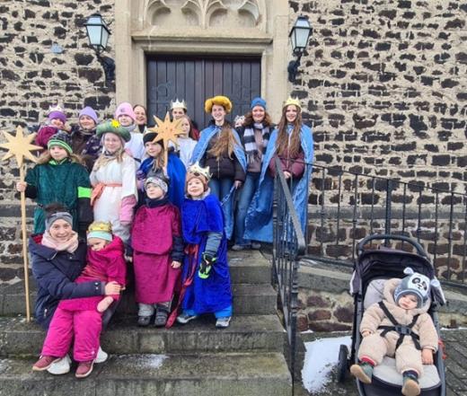 Man sieht eine Gruppe Kinder als Sternsinger verkleidet vor einem Kirchenprotal