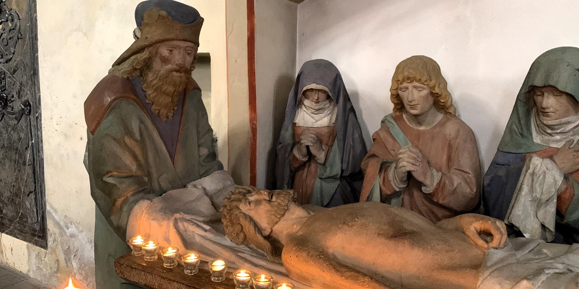 Man sieht die steinerne Grablegungsgruppe in der Kirche in Münstermaifeld mit Kerzen geschmückt