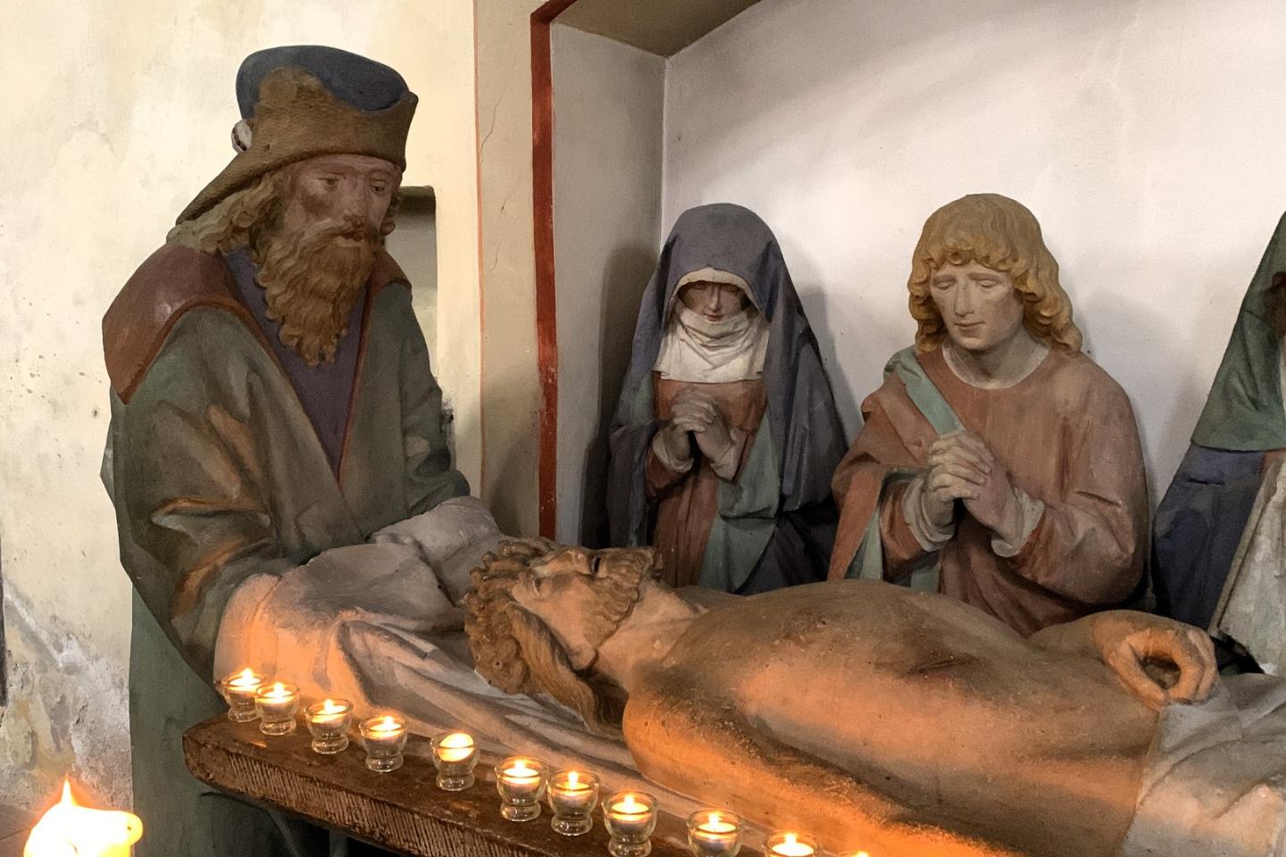 Man sieht die steinerne Grablegungsgruppe in der Kirche in Münstermaifeld mit Kerzen geschmückt
