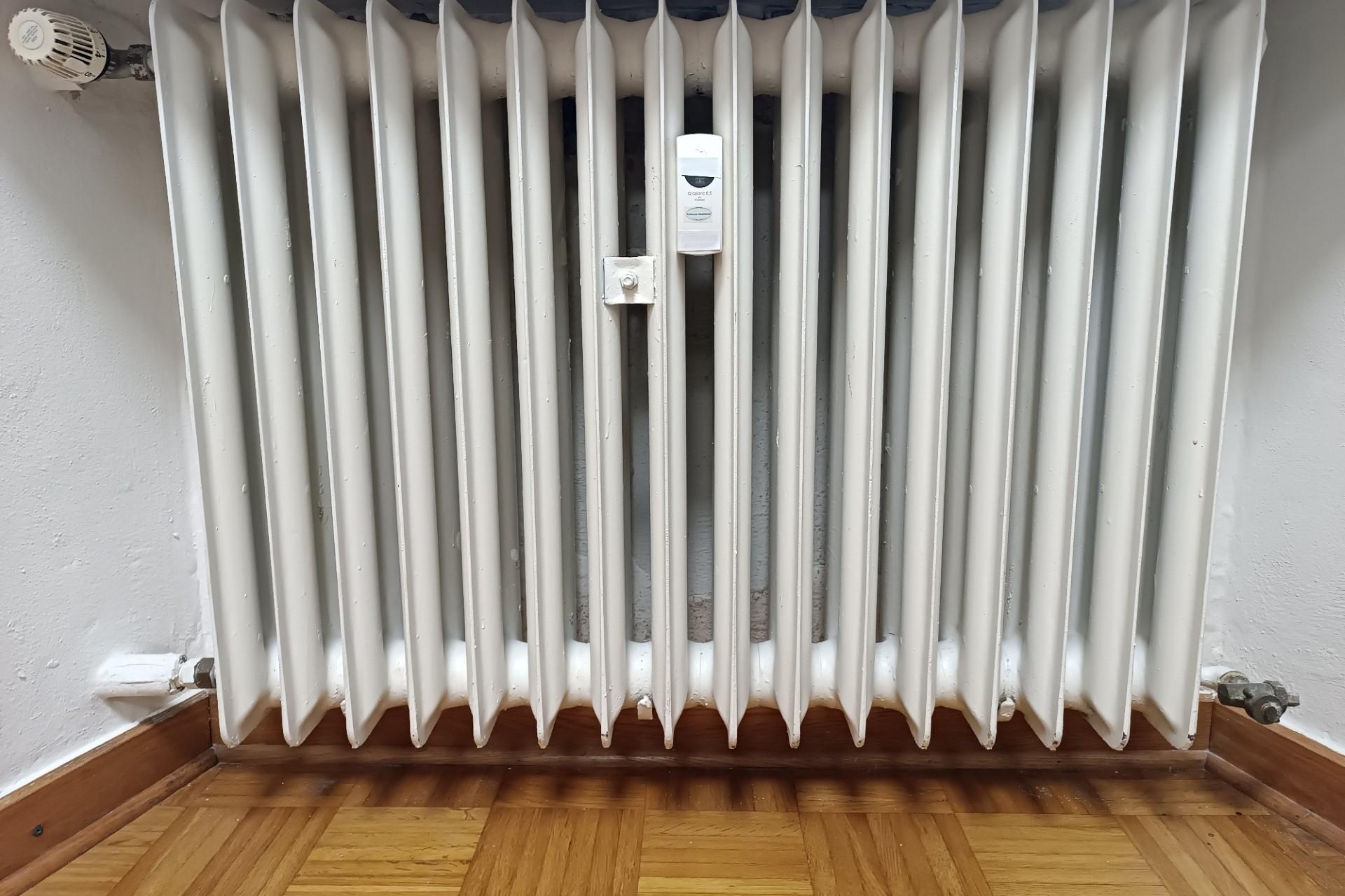 Man sieht einen alten, weißen Heizkörper in eine Mauernische eingelassen, darunter Parkettboden