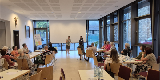 Man sieht zwei Frauen im Vordergrund, die eine Veranstaltung moderieren und Menschen, die an Tischen sitzend, der Veranstaltung lauschen (c) Pastoraler Raum Maifeld-Untermosel/Privat Man sieht zwei Frauen im Vordergrund, die eine Veranstaltung moderieren und Menschen, die an Tischen sitzend, der Veranstaltung lauschen