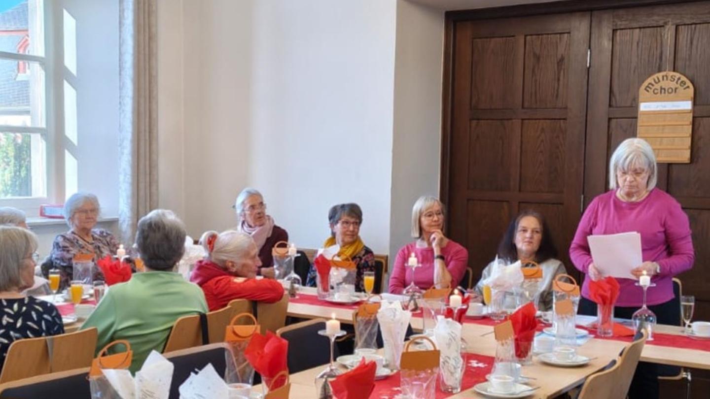 Man sieht Frauen an einem langen Tisch sitzend, einer vortragenden Frau zuhören
