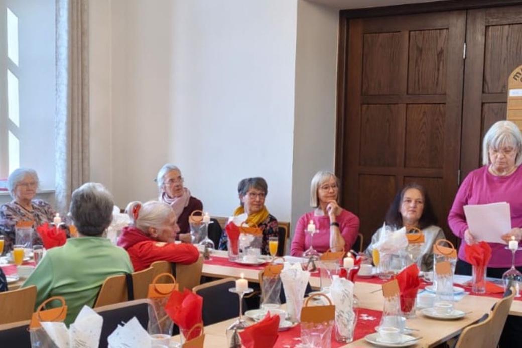 Man sieht Frauen an einem langen Tisch sitzend, einer vortragenden Frau zuhören