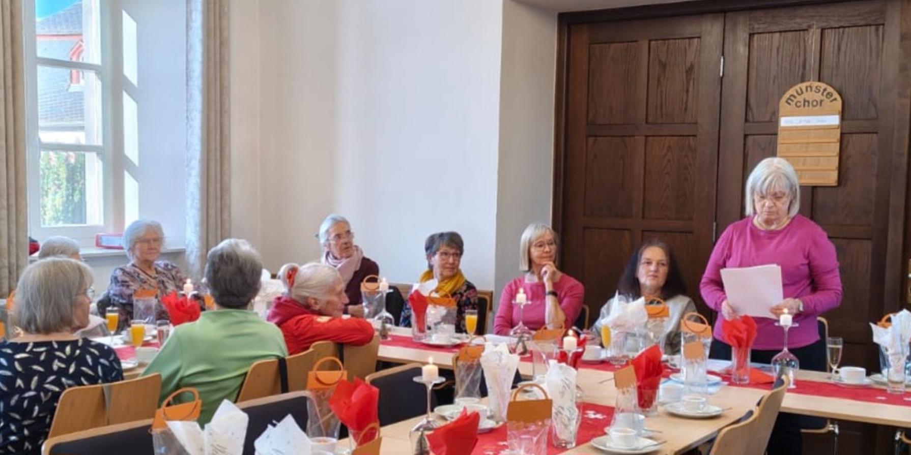 Man sieht Frauen an einem langen Tisch sitzend, einer vortragenden Frau zuhören