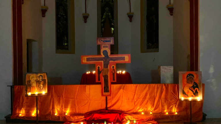 Man sieht den mit Kerzen und Tüchern geschmückten Altarraum der abgedunkelten Josefskapelle, davor Ikonen-Kreuze