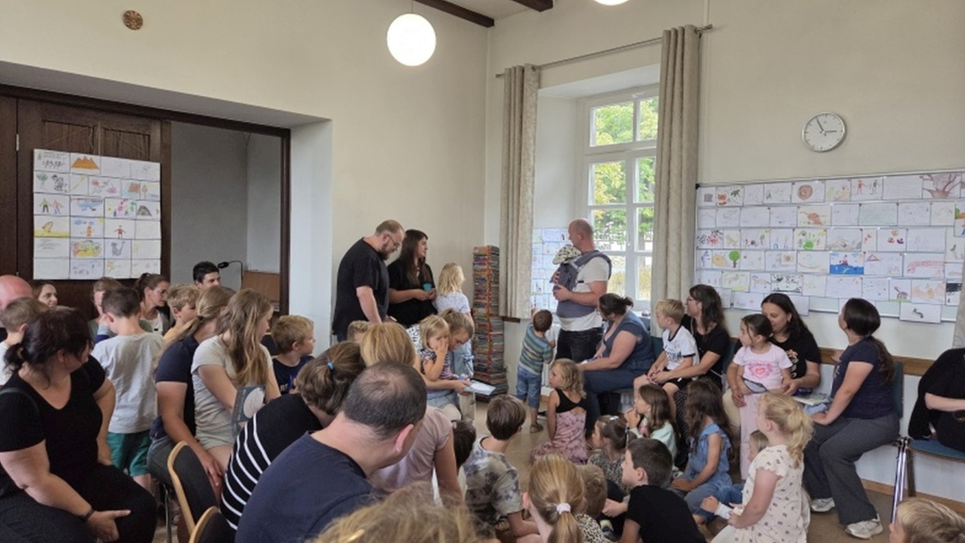 Man sieht Kinder und Eltern, die in einem Pfarrsaal beieinander sitzen