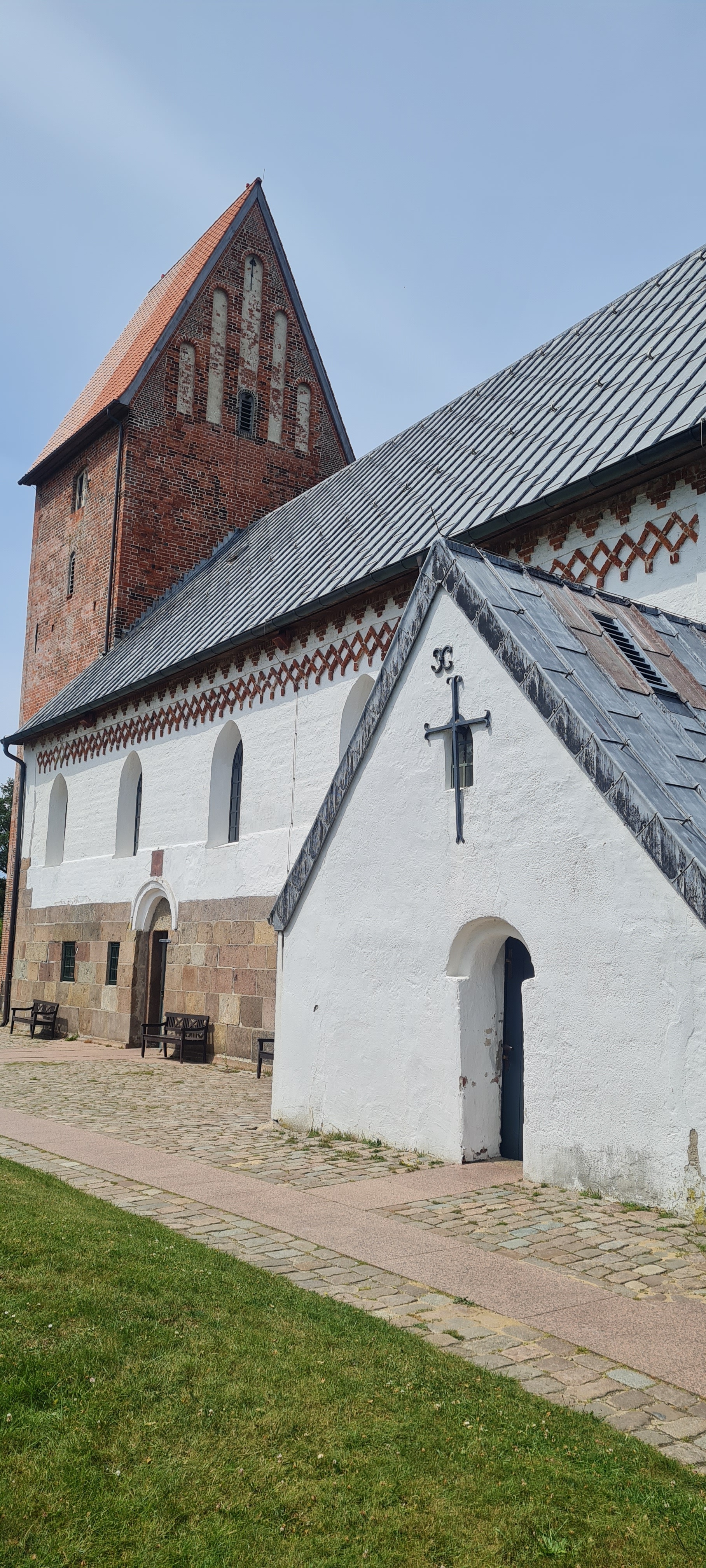 Man sieht die weiße Außenansicht der Kirche mit in roten Ziegelsteinen angebautem Kirchenturm