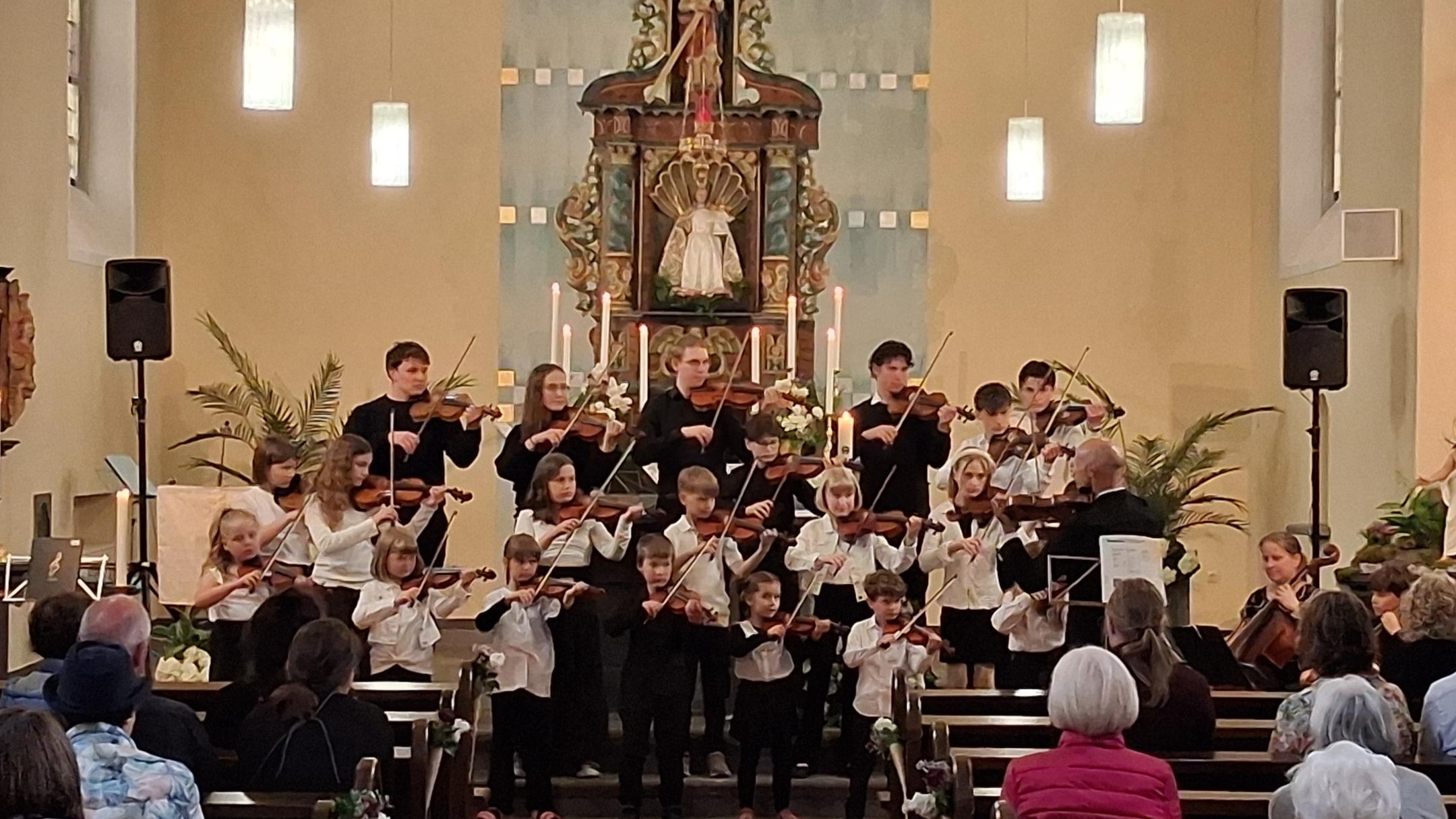 Man sieht den Altarraum mit Hochaltar der Kirche in Kalt, in dem ein Orchester aus Streichern, Kinder und Erwachsene stehen