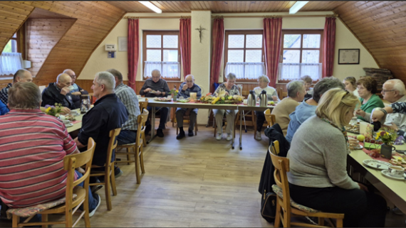 Man sieht einen Saal in dem Menschen Kaffee trinken und Kuchen essen