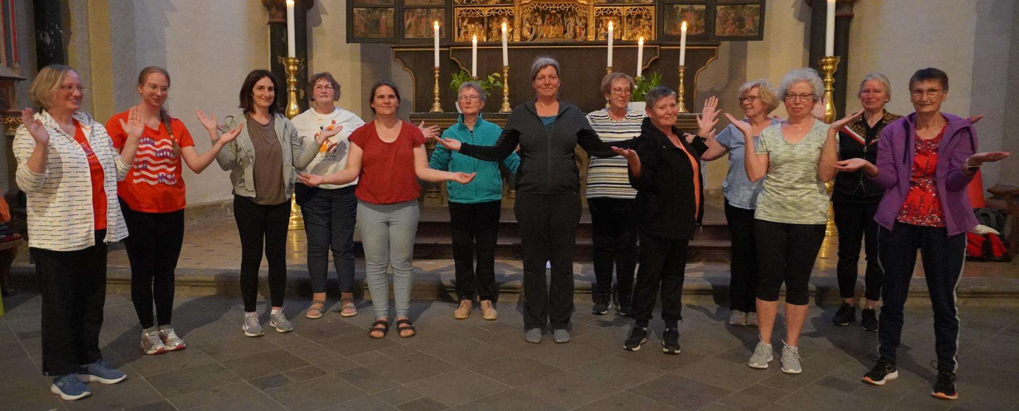 Man sieht Frauen im Sportdress vor einem Altar stehen, die Hände wie zum Gebet geöffnet