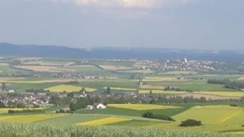 Das Bild zeigt einen weiten Blick über die Frühlingslandschaft mit gelb blühenden Rapsfeldern im Maifeld