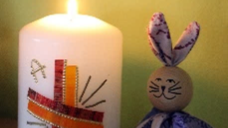 Man sieht einen Osterhasen neben einer Osterkerze sitzen