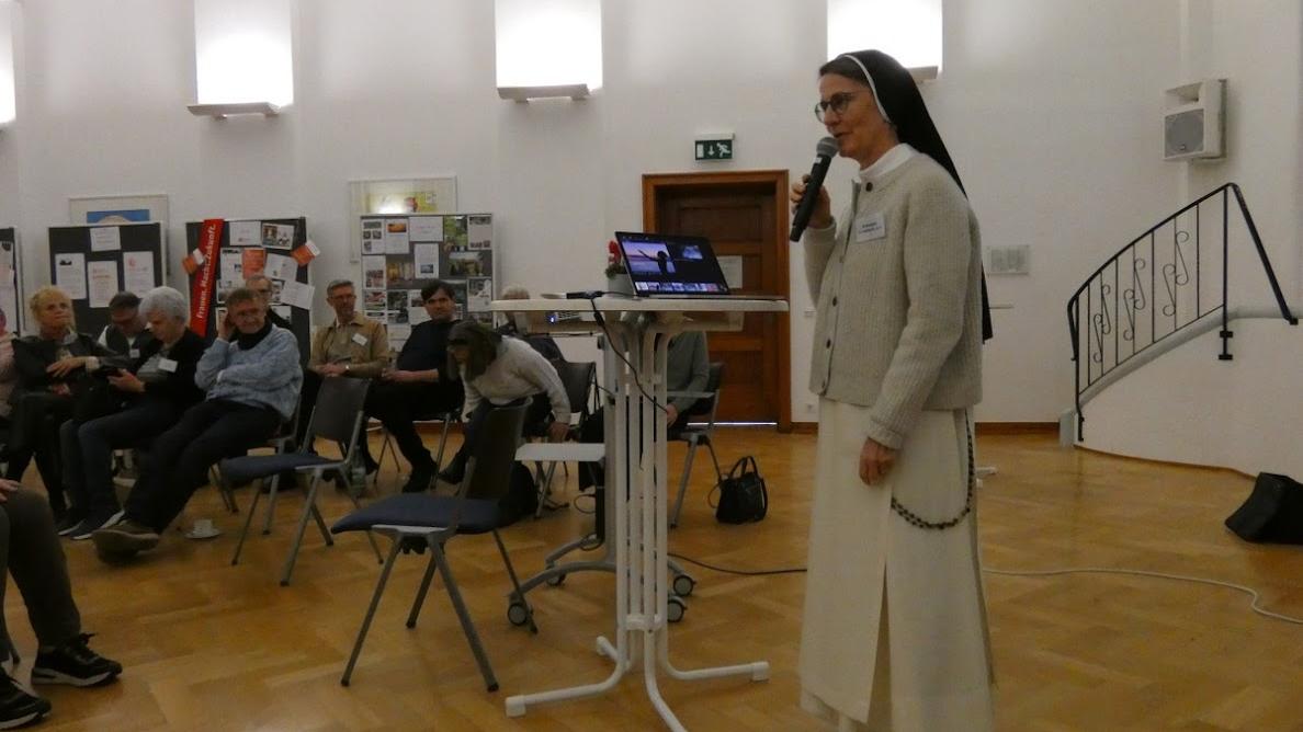 Man sieht eine Ordensschwester, die einen Vortrag vor Publikum hält