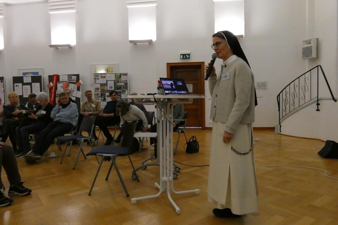 Man sieht eine Ordensschwester, die einen Vortrag vor Publikum hält