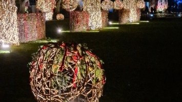 Man sieht einen beleuchteten Uferstreifen bei Dunkelheit, davor eine Rebenkugel, die mit bunten Lichtern geschmückt ist