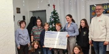 Man sieht eine Gruppe Menschen, die einen Spendenscheck halten, in einem Wohnzimmer (c) Edith Valentin-Gärtner Man sieht eine Gruppe Menschen, die einen Spendenscheck halten, in einem Wohnzimmer