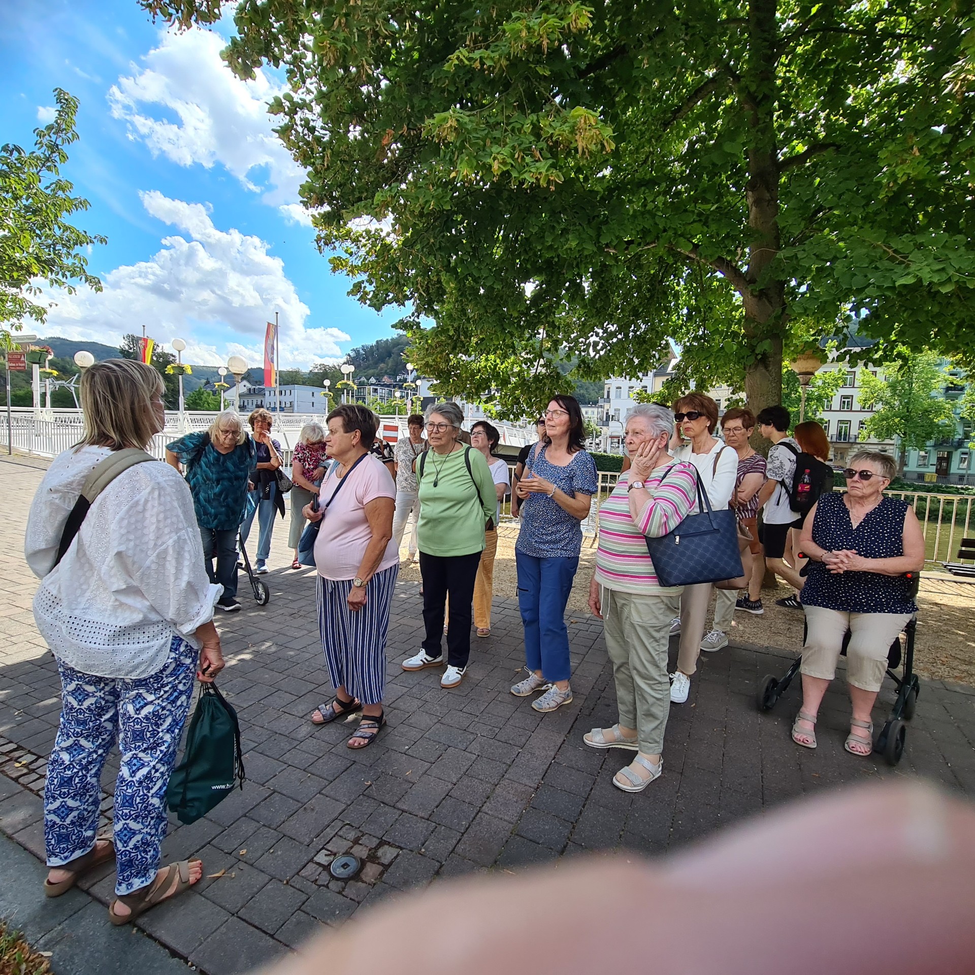Man sieht Frauen am Ufer eines Flusses stehen, darüber blauer Himmel mit weißen Wolken