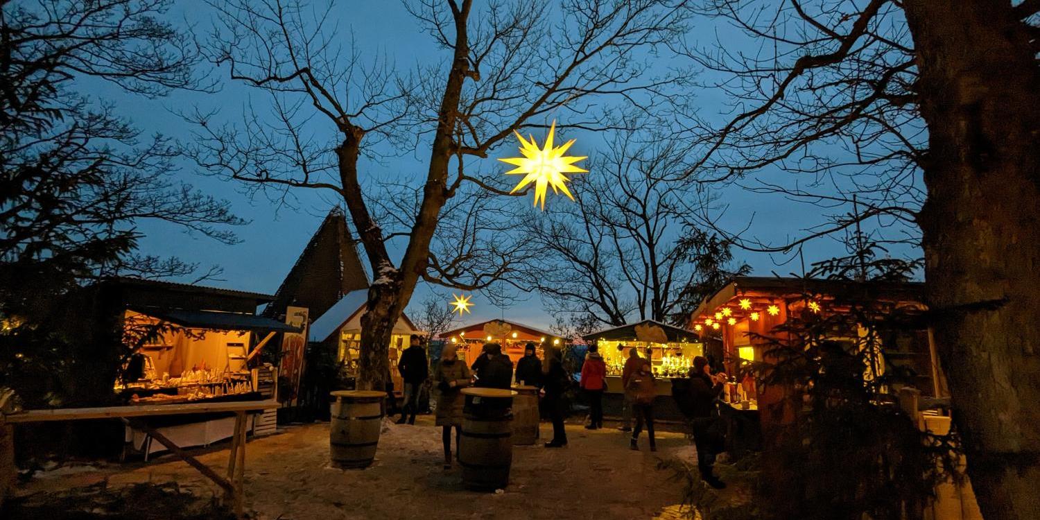 Man sieht einen gut besuchten Weihnachtsmarkt mit Beleuchtung und Ständen