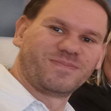 Man sieht das Foto eines jungen Mannes mit braunen Augen und dunklem Haar, einen Anzug und ein weißes Hemdtragend