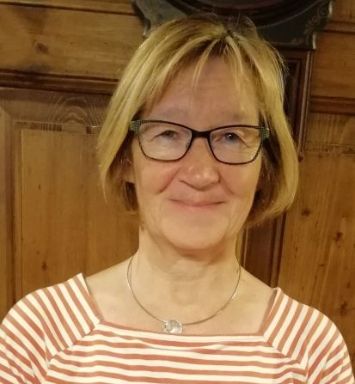 Man sieht eine Frau mit Brille, blondem Haar  und Ringelpulli vor einem Schrank stehend